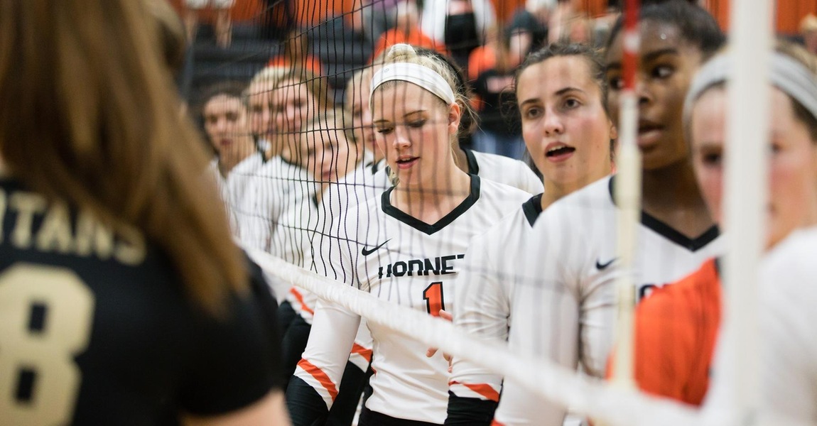 Kalamazoo College volleyball players at the net.
