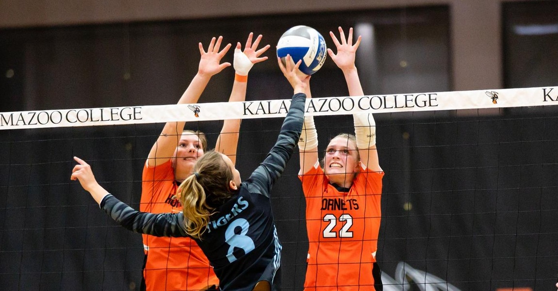 Kalamazoo College volleyball players going up for a block.